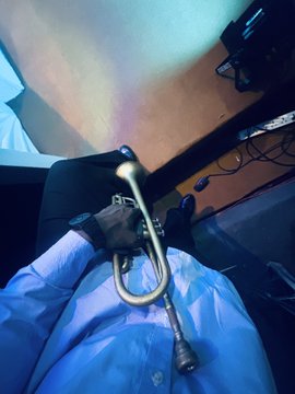 A first-person perspective shows a person holding a vintage-style metal hand pump or device over blue protective covering, with a wooden floor visible in the background.