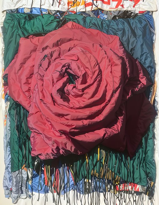 An art piece features a large red rose crafted from crumpled fabric or paper, set against a background of green and blue materials with paint drips.