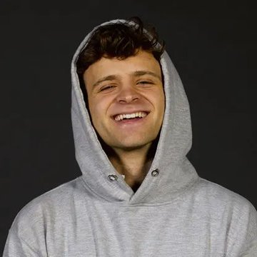 A young man in a gray hoodie smiles broadly against a dark background, with the post describing Jack Mallers' Strike launching volatility-proof Bitcoin-backed loans that allow users to borrow cash without risking liquidation from price crashes.