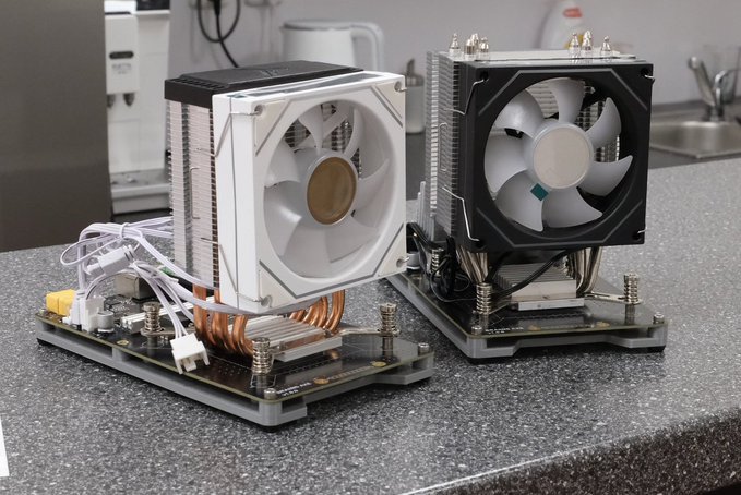 Two Braiins Mini Miner BMH 100 devices with exposed cooling fans and circuitry are placed side by side on a granite countertop, showing their internal heatsinks and wiring.