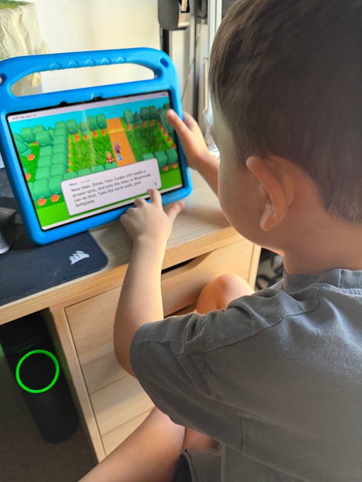 A young child sits focused on a tablet displaying a colorful, pixelated game world, engaging with what appears to be the Lumena game experience. The setup illustrates how the game is designed to be intuitive and enjoyable for players of any age, reinforcing the post's message about accessibility for "the youngest trainer yet."