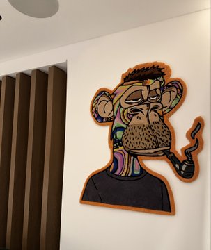 A colorful street art style painting of a monkey smoking a pipe, displayed on a white wall next to wooden slats.