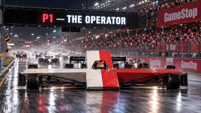 A dramatic racing game screenshot showing an open-wheel race car on a wet track, with the scoreboard reading 'P1 — THE OPERATOR' and GameStop banners in the background.