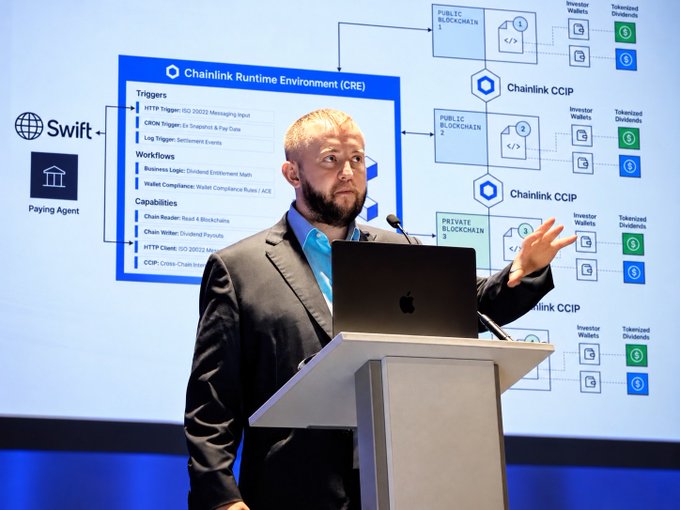 A man with a beard and glasses presenting at a podium with a laptop, standing in front of a detailed technical diagram explaining 'Chainlink Runtime Environment (CRE)' and 'Chainlink CCIP'.