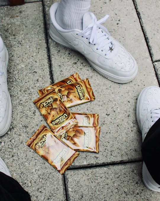 Two pairs of feet in white sneakers surround several packs of condoms scattered on a concrete pavement.