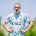 The image features a man wearing a white soccer jersey with the word "Kiwi" written across the front of it, standing outdoors against a green background. The man appears to be looking off into the distance or posing for a photo while holding his hands up in the air. There is also text present in the image that reads "@okx 世界杯预测活动大家都可以参与进来".