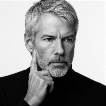 A black-and-white portrait of a silver-haired, bearded man resting his hand thoughtfully against his cheek, wearing a dark turtleneck against a plain white background. The contemplative pose visually reinforces the post's reference to Michael Saylor and his forward-looking strategic analogy about $MSTR and the newly launched $STRC preferred instrument.