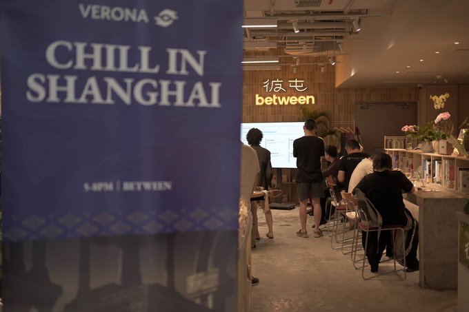 A banner reading "VERONA CHILL IN SHANGHAI 5-6PM | BETWEEN" stands prominently in the foreground, while attendees gather in the background at an event titled "彼屯 between," where speakers BurntBanksy and PhilGeorge discussed user-owned verification and ero's role in turning proof into spendable money.