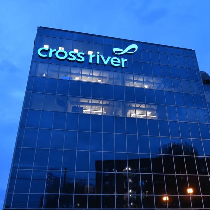 The illuminated "Cross River" logo is displayed atop a modern glass office building at dusk, representing Cross River Bank, the institution that has integrated Ripple's Ethereum stablecoin into its institutional payments operating system in the US.
