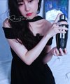 A person with long dark hair wearing a black dress, holding an object and looking downward, with an illegible watermark on the image.