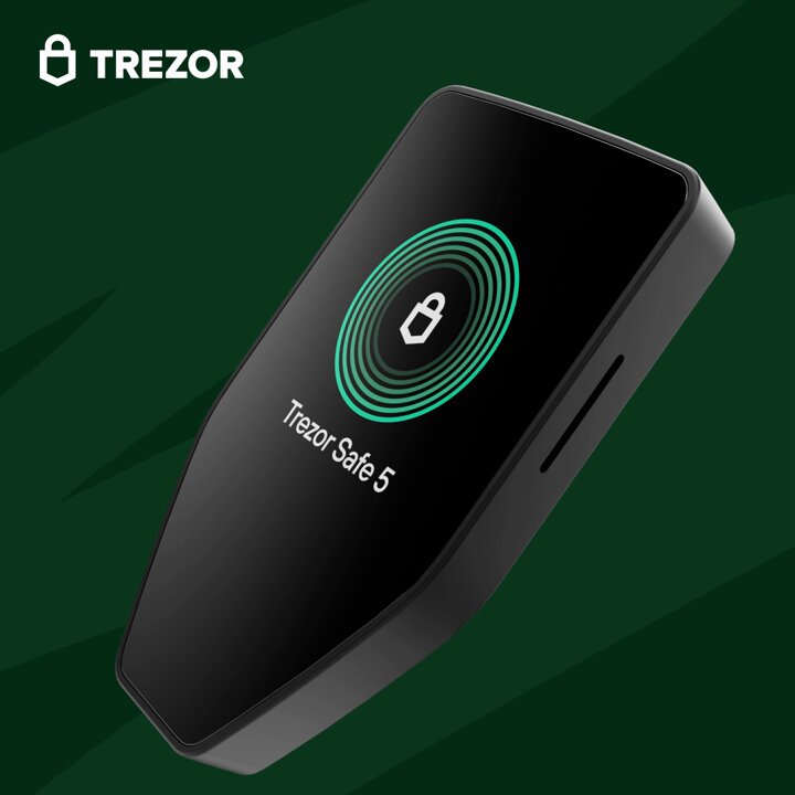 The image features a black Trezor phone with a green lock screen, which has the text "Trezor Safe 5" displayed prominently. The phone appears to be turned off or in standby mode. In the background of the image, there is a green color that blends into the overall design and makes it difficult to see any other objects or details beyond the phone's screen.
