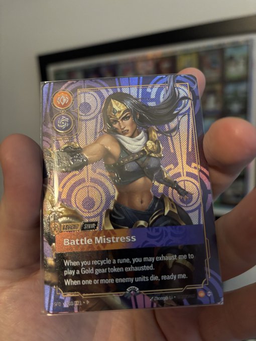 A hand holds a holographic foil Riftbound TCG "Battle Mistress" Legend card featuring a fierce warrior woman with flowing dark hair. The card, marked SFD 003/023, is one of six metal cards being sent to BGS for grading.