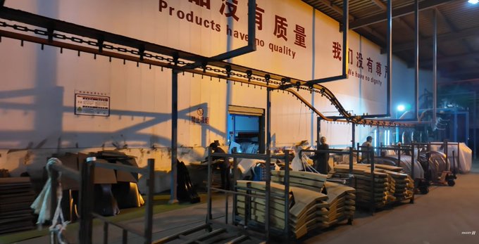 The image shows a large warehouse with several stacks of cardboard boxes, indicating that this could be an industrial setting or a storage area for goods. The photo also features a sign written in Chinese characters, which suggests that the location might be in China or have some connection to Chinese culture. The overall atmosphere seems to be focused on work and productivity rather than excitement or hype.