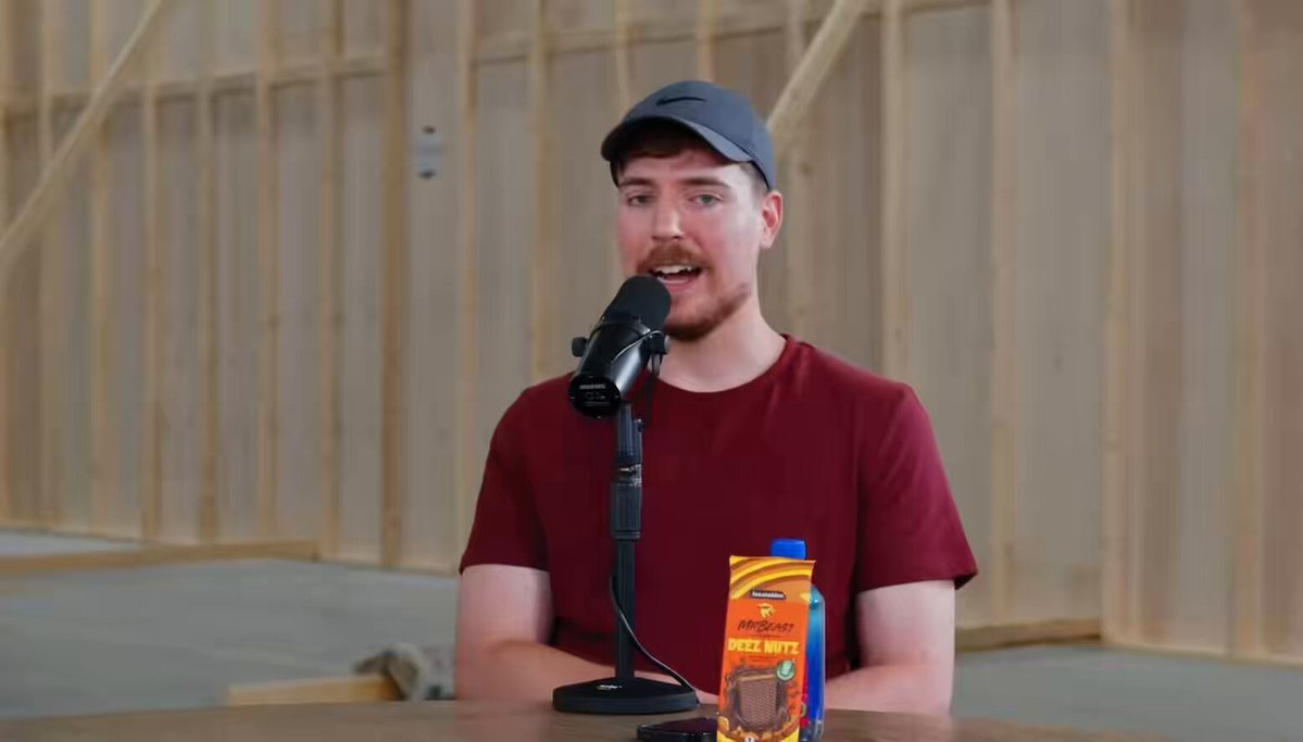 The image features a man wearing a red shirt, sitting at a table with a microphone in front of him. He appears to be speaking into the microphone or possibly recording something. On the table next to him, there are two items - an orange juice box and a bag of cookies. The text on the post reads "This gets me bullish as fuck on the content we have about to cook for $WAGMI Literally just fucking knowledge baby". This suggests that the man might be discussing cooking or food-related topics in his speech, possibly related to the orange juice and cookies he has nearby.