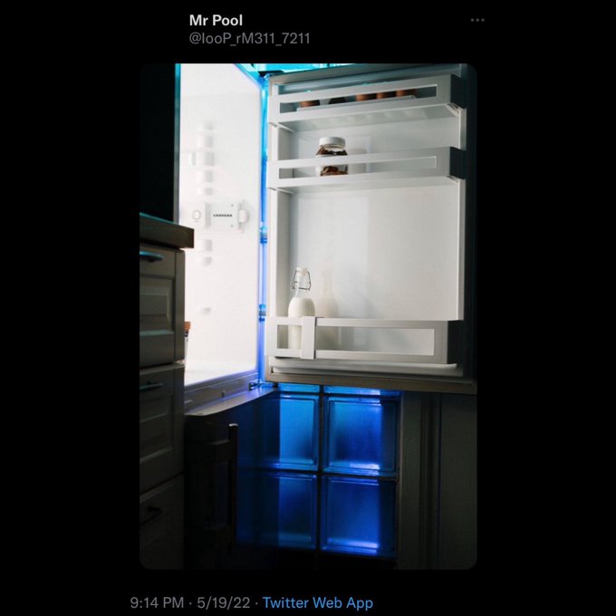 An open Samsung refrigerator is shown nearly empty except for a small bottle and jar on the shelves, with its lower drawers illuminated by blue light. The image relates to the accompanying post about an empty fridge because "everything is in XRP," humorously suggesting the owner spent their money on cryptocurrency rather than groceries.