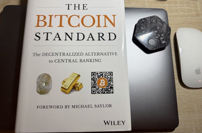 A copy of the book 'The Bitcoin Standard: The Decentralized Alternative to Central Banking' with a foreword by Michael Saylor, sitting next to an Apple Magic Mouse on a desk.
