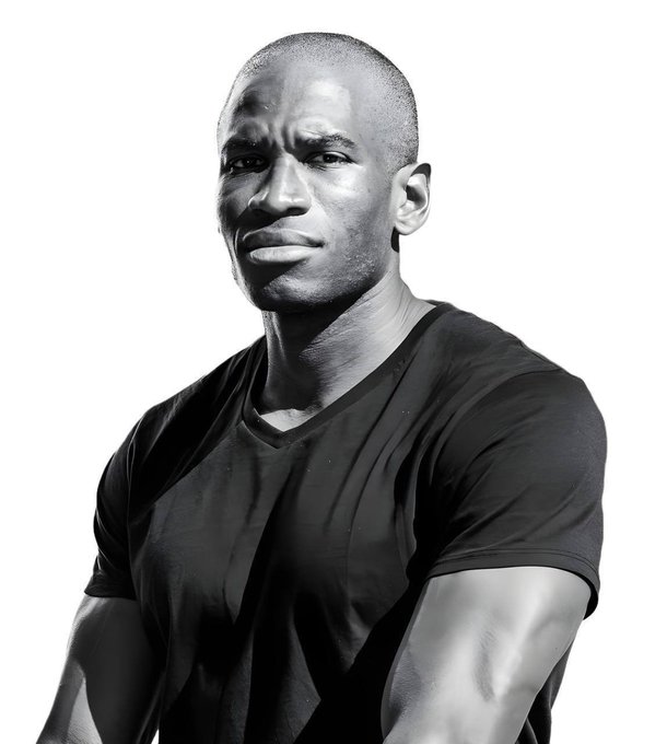 A black and white portrait of a muscular man with a shaved head wearing a tight black v-neck t-shirt.