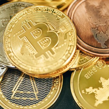 A close-up view of physical cryptocurrency coins, prominently featuring a gold Bitcoin with the visible inscription "BITCOIN DIGITAL · PEER TO PEER" alongside copper and silver-colored altcoin tokens, visually representing the growing ranks of crypto wealth mentioned in the post about 135,694 crypto millionaires and 23 billionaires worldwide.