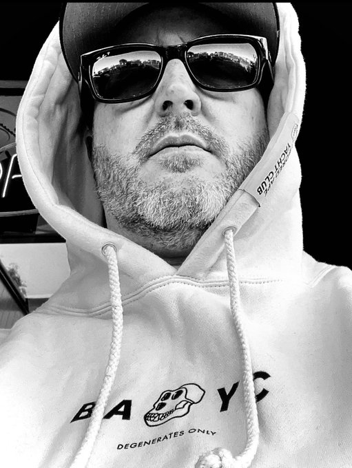A black-and-white selfie shows a bearded man wearing sunglasses (reflecting a cityscape) and a white hoodie featuring a skull design with the text 'BANG YCD DEGENERATES ONLY'.