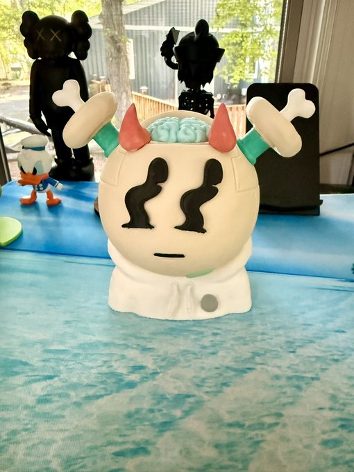 A person displays their "QUIRKIE" collectible figure—a white skull-like character with red horns, bone-shaped ears, and an exposed brain—sitting on a wave-patterned towel, while the accompanying post expresses gratitude to @polkadothodler for the gift and embraces the playful "QUIRK LIFE" theme.