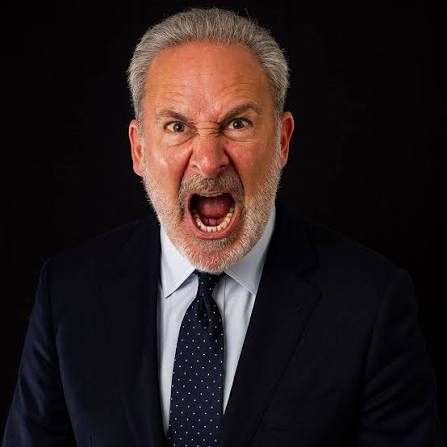 A man with gray hair and beard wearing a dark suit and tie yells angrily with his mouth wide open against a black background.