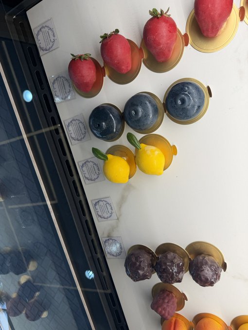 An elegant display of fruit-shaped chocolates (strawberries, blueberries, lemons, and others) arranged in rows on gold bases.