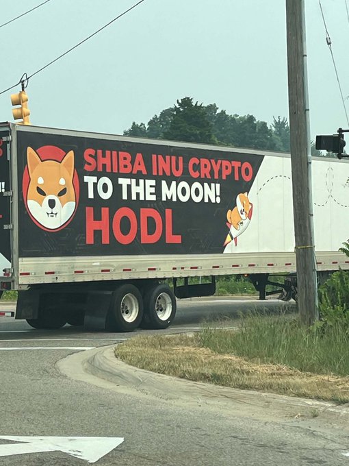A truck trailer displays a large advertisement featuring a Shiba Inu dog with the text 'SHIBA INU CRYPTO TO THE MOON! HODL' alongside a rocket illustration.