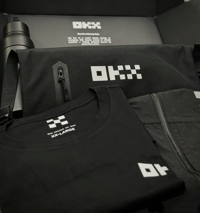An OKX branded apparel set is displayed in its packaging, including a black duffel bag, t-shirt, and pants all featuring the OKX logo, with a water bottle also visible.