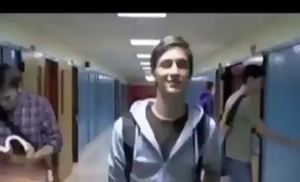 The image features a hallway with three people walking down it, including one person wearing a backpack. One of the individuals appears to be smiling at the camera while they walk. The caption for this image reads "This might be the greatest video ever".