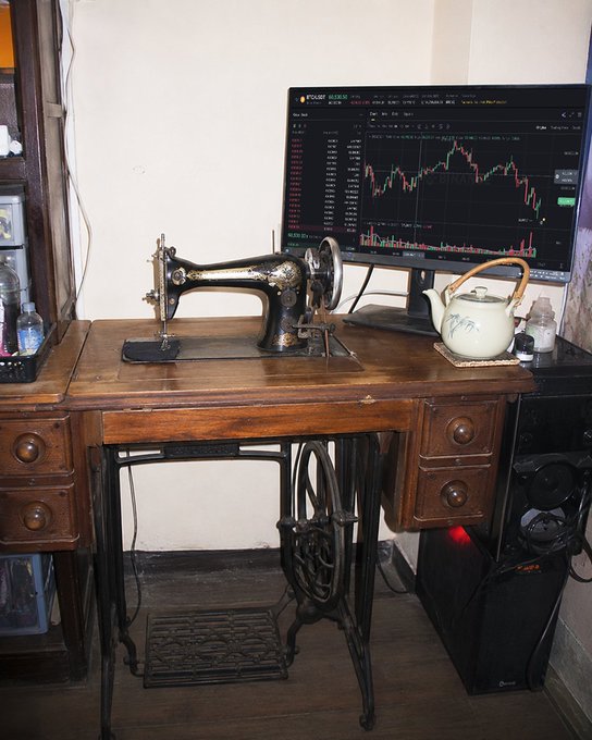 An antique cast-iron sewing machine sits on a vintage wooden treadle table beside a modern monitor displaying a colorful cryptocurrency trading chart for "BTC/USDT" on the Poloniex exchange, alongside a decorative teapot. The "grandma's setup" caption humorously reflects the eclectic combination of heirloom craftsmanship and contemporary trading technology sharing the same workspace.