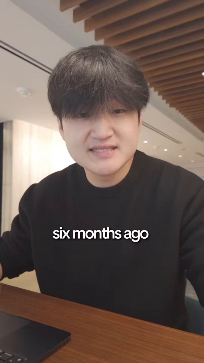 The image features a man sitting at a desk with a laptop computer, wearing a black sweater. The background of the photo shows a wooden wall with a window. There are also some words written below the image that read "Six months ago." This suggests that the image was taken in the past and is related to Claude Code or his work as an AI developer.