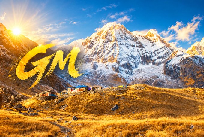 A scenic mountain landscape with snow-capped peaks, a small village, and golden grass under a blue sky, overlaid with yellow text reading 'GJM'.