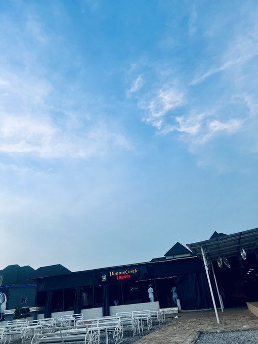 A photograph taken from a low angle shows an outdoor venue with picnic tables and a black building labeled 'DimmsCastle LOUNGE' under a blue sky with scattered clouds.