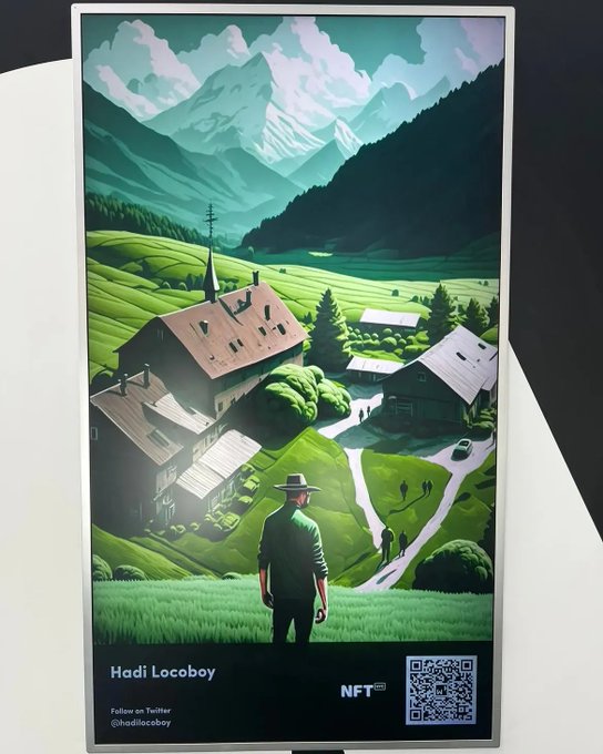 A digital illustration displayed on a screen showing a scenic Alpine village with a man in the foreground, labeled 'Hadi Locoboy' with an NFT logo and a QR code, along with text 'Follow on Twitter @hadilocoboy'.