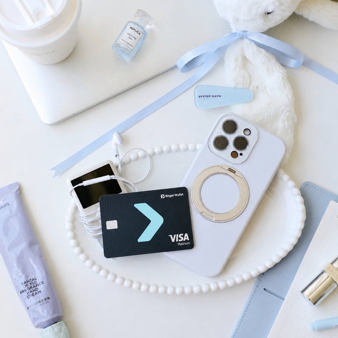 A flat lay featuring a "Bespoke Wallet" Visa Platinum debit card by Banqet, displayed alongside a white iPhone with a magnetic ring holder, pearl necklace, a teddy bear, a laptop, lip balm, and a hand cream labeled "Santa Juice Fragrance Hand Cream." The post's "main character" theme is reflected through the neatly styled personal items, with the sleek Visa Platinum debit card positioned as the centerpiece of this curated, aesthetically pleasing lifestyle moment.