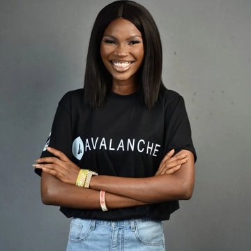 A smiling woman stands with her arms crossed, wearing a black t-shirt featuring the "AVALANCHE" logo, celebrating her acceptance as a collaborator with the Avax team. Her excited expression and branded apparel reflect her enthusiasm for joining the Avalanche crypto community.