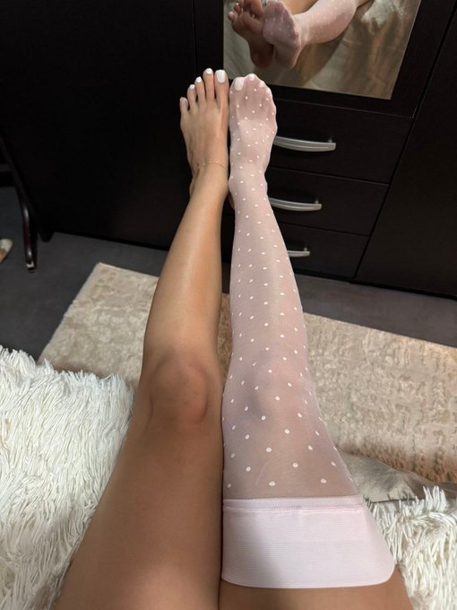 A first-person view showing one bare leg next to another wearing a white polka-dot sheer stocking.