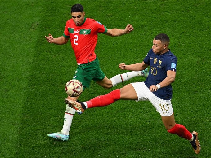 Soccer players from Morocco and France compete for the ball during a match on a green field.