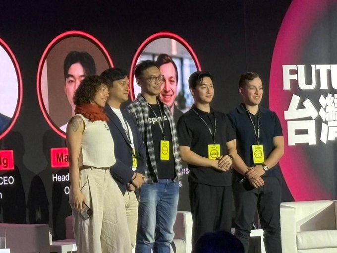 A group of five people standing on stage at what appears to be a panel or conference, wearing yellow badges, with 'FUTURE' text visible in the background alongside Chinese characters.