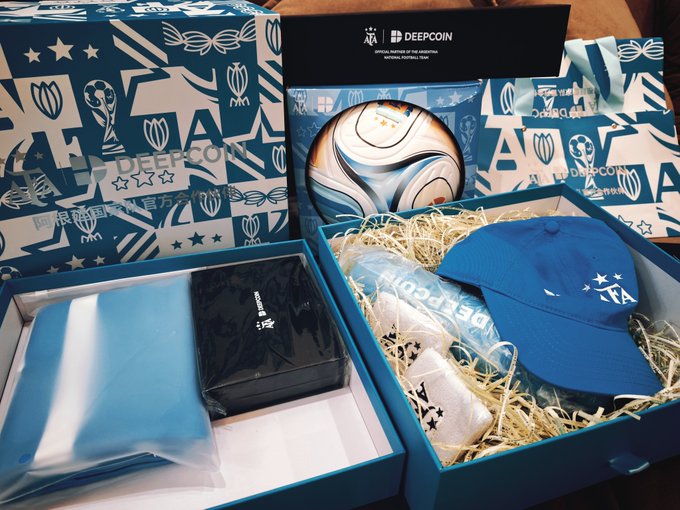 Deepcoin Argentina national football team co-branded merchandise gift box featuring a soccer ball, blue cap with stars, and branded accessories displayed with packing straw and packaging marked "OFFICIAL PARTNER OF THE ARGENTINA NATIONAL FOOTBALL TEAM."