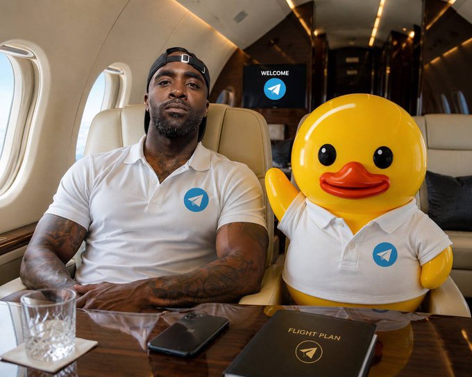 A man in a white polo shirt and a yellow duck mascot, both with Telegram logos on their shirts, sitting inside a private jet with a 'WELCOME' screen and a 'FLIGHT PLAN' booklet on the table.