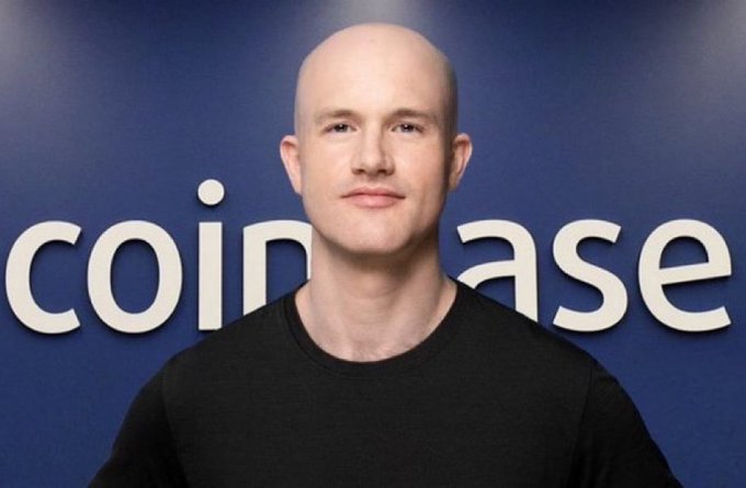 A bald man wearing a black t-shirt stands in front of a blue backdrop displaying the "coinbase" logo. The image connects to the post by referencing Coinbase's involvement with U.S. Treasury and Commerce Departments in advancing a strategic Bitcoin reserve.