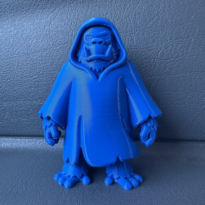 A photo of a blue 3D-printed figurine depicting a hooded, masked creature with claws and large feet, sitting against a gray background.