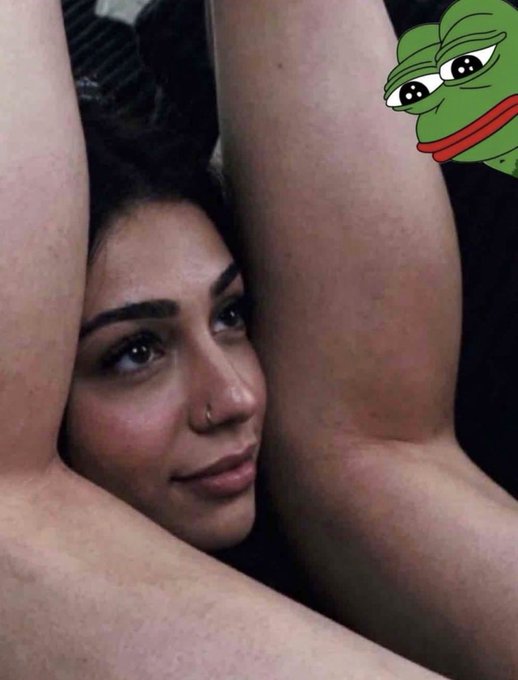 A woman with dark hair rests her head between her raised legs in a selfie pose, with a Pepe the Frog sticker placed in the upper right corner.