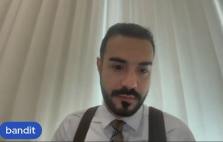 A man with a beard, wearing a white shirt, tie, and suspenders, looks directly at the camera in a video call setting, with the word 'bandit' displayed in a blue badge in the corner.