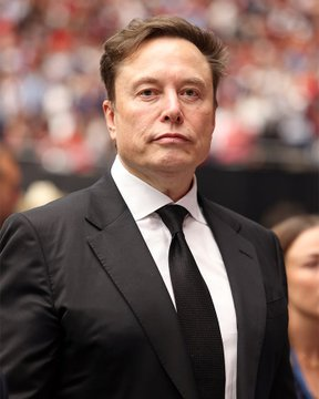 A man in a black suit and tie with short brown hair looks off to the side at what appears to be a crowded event with people in red visible in the background. The image accompanies a post about Elon Musk endorsing Bitcoin as a superior store of value compared to traditional fiat currency, suggesting the man pictured is Elon Musk making this statement.