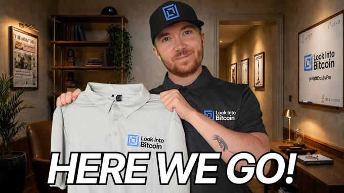 A man wearing a black 'Look Into Bitcoin' cap and shirt holds up a white branded polo shirt, with the text 'HERE WE GO!' overlaid at the bottom.