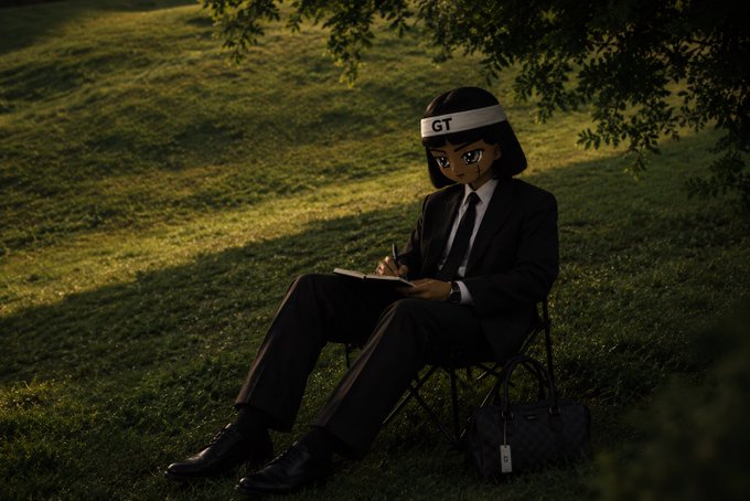 A 3D-rendered anime-style character with short black hair wearing a black suit and a white headband labeled 'GT' sits on a chair under a tree in a grassy field, writing in a notebook with a designer handbag beside them.