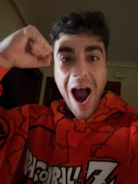 A young man wearing a red Dragon Ball Z t-shirt with an excited expression and a raised fist, appearing to be reacting enthusiastically.