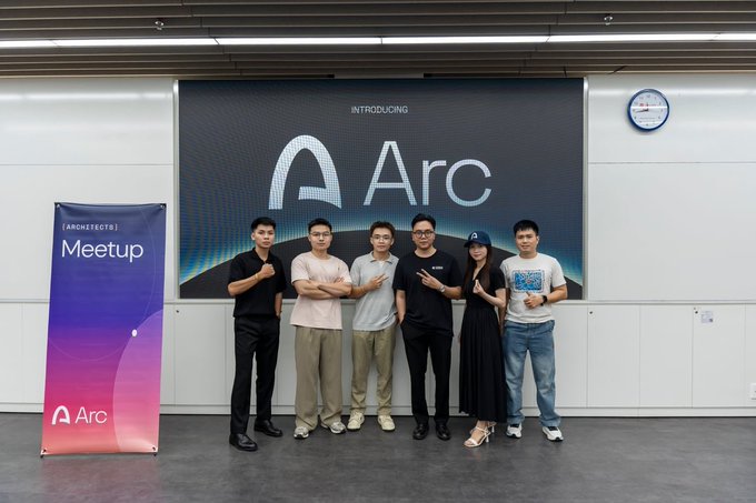 A group of six people posing in front of a large screen introducing 'Arc' at an 'Architects Meetup' event, with a branded banner standing to the left.